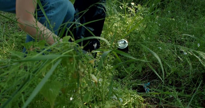 Volunteer picking up trash from grass in forest. Earth Day or Environment Day