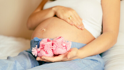 Pregnancy baby shoes. Happy pregnant woman holding pink baby shoes. Small child shoe. Concept of pregnancy, maternity, expectation for baby birth.