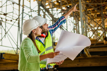 Woman architect and men contractor examining plans on construction site.