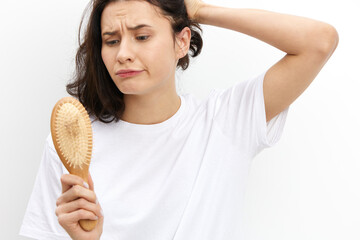 a sad, upset woman stands holding her head in panic and looks at a wooden massage comb