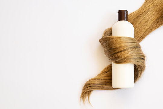 Shampoo bottle wrapped in hair lock on white background, flat lay with space for text. Natural cosmetic products