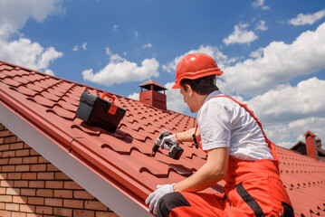 Man worker master in red overall and helmet is fixing the metal tile roof.