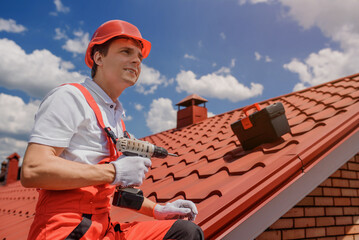 Man worker master in red overall and helmet is fixing the metal tile roof.