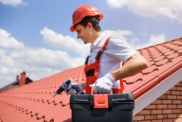 Man worker master in red overall and helmet is fixing the metal tile roof.