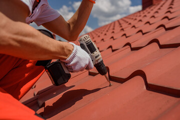 worker master hands holding an electric screwdriver and fixing the metal tile roof.