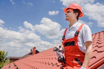 Man worker master in red overall and helmet is fixing the metal tile roof.