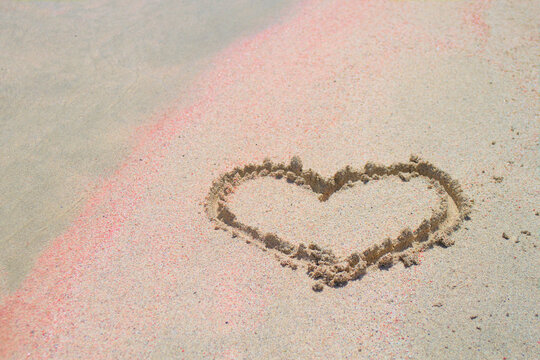 A painted heart on pink sand. Symbol of love