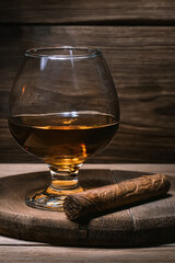 Cognac glass background. glass of cognac stands on wooden oak stand, next to cigar lies close-up...