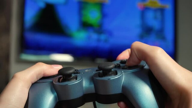 Teenager playing a video game on the console. Gamepad in hand, presses the buttons, close-up.