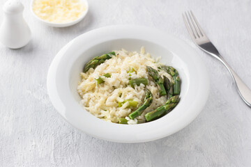 White plate of delicious creamy risotto with asparagus and cheese on a light gray background. traditional italian food
