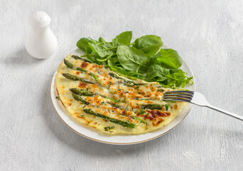 Delicious omelette with asparagus and cheese on a white plate on a light gray background, top view....