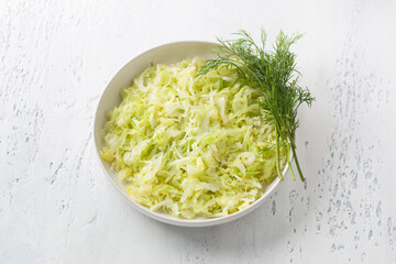 Steam white cabbage in a white ceramic bowl with herbs and green sauce on a light blue background, top view. Delicious diet food