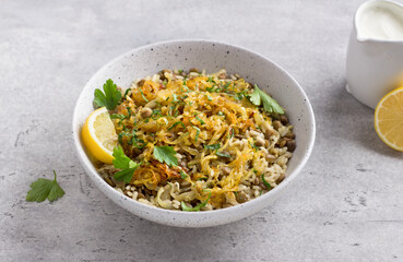 Traditional Middle Eastern dish, Mujadara of lentils, rice and fried onions with lemon and herbs on a light gray background