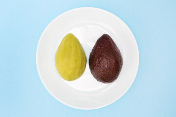 Avocado cut in half, one part without peel. Ripe avocado fruit in a plate on a blue background. Food for a healthy diet. Flat lay. Top view. Slimming product.