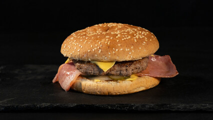 Delicious homemade hamburger, beef, bacon, cheese, on a black background