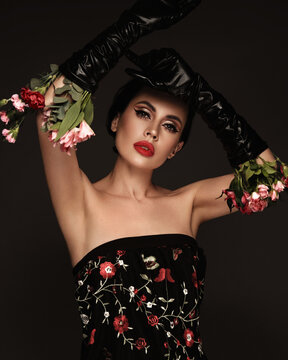 Beautiful brunette woman iwith a classic make-up, red lips, holding flowers. The beauty of the face.