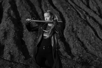 Beautiful woman in leather jacket with vintage sword in black and white
