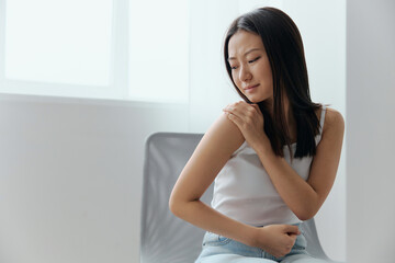 Suffering from neuralgia after sleeping in the wrong position tanned beautiful young Asian woman touching painful shoulder at home living room. Injuries Poor health Illness concept. Cool offer Banner