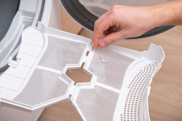 A man takes a lint filter out of the dryer and cleans it from dust, lint, hair, wool.
