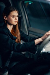 Fototapeta na wymiar vertical portrait of a frustrated woman sitting in a car at night behind the wheel wearing a seat belt