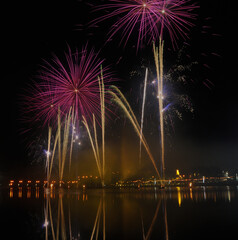 Fogo de artifício disparado de plataformas á tona da água de um rio com efeito de espelho na água