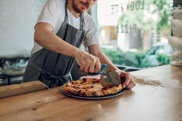 Hand of kitchen chef cutting pizza with a pizza cutter