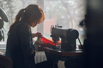 Tailor woman sitting and sewing on a sewing machine a in studio