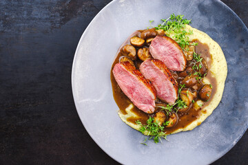 Barbecue gourmet duck breast filet with polenta and caramelized mushrooms in hearty beer sauce served as top view on a design plate with copy space left