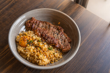 selective focus, beef fat garlic ​fried rice with​ ​beef steak ​and topping with pickled egg yolk in a bowl on wooden table. Grilled Meats, thai is menu is fusion food.