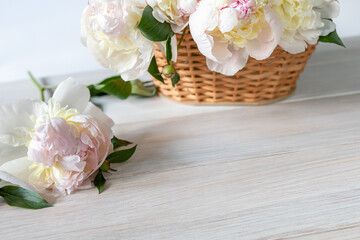 Light peonies in a wicker basket on a white wooden table