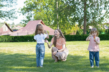 Obraz premium Mom and two daughters have fun playing in the park and blowing soap bubbles.