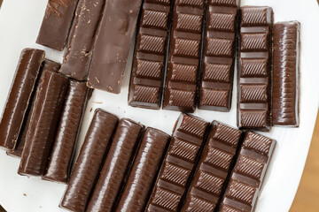 Close up of various dark chocolate bars on a white plate. Wooden table