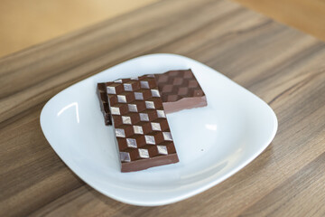 Two dark chocolate bars on a white plate. Wooden table