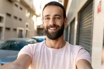 Fototapeta premium Successful happy hispanic influencer recording video using modern technology outdoors. Handsome smiling man tourist taking selfie on the street. Vacation, travel concept 