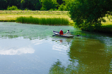 Boat with people on the pond. A man rows a boat on a lake surrounded by trees, while his wife...