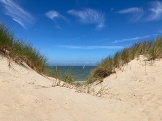 Fototapeta na wymiar Sommerliche Dünenlandschaft an der Nordseeküste mit Sand und Strandhafer vor blauem Himmel mit Cyrruswolken bei de Haan, Belgien