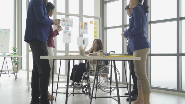 Disabled people with a group of Asian business team talk, communicate, discuss, and work in meeting room office, present ideas to colleagues. People lifestyle. Corporation