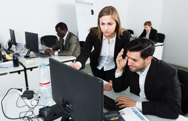 Unhappy man manager working at laptop and angry woman boss pointinting to misses in work. Focus on...