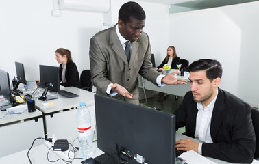 Man manager working at laptop and angry male boss pointinting to misses in work.