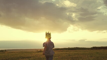 little child boy runs across field with crown head. superhero sun glare light. happy childhood...