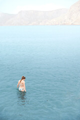 Young adult woman in bikini enters the Mediterranean Sea alone to swim while the water is calm and nobody bothers her. Relax image. Moments of introspection