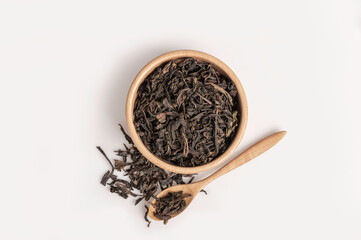 Dry black tea in a wooden bowl and spoon isolated on white background.