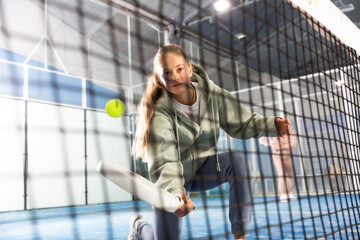 Teenage girl holding padel racquet in hand and ready to return ball while playing in court.