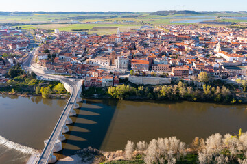Fototapeta premium Picturesque aerial view of Tordesillas townscape on Duero river overlooking brownish tiled roofs of residential buildings and temples on spring day, Spain