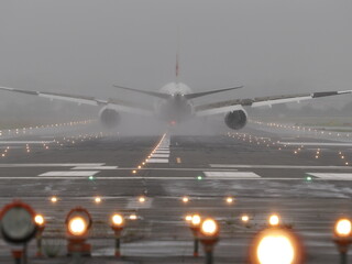 雨天の誘導灯が点灯した滑走路に着陸した旅客機の下方衝突防止灯と尾灯