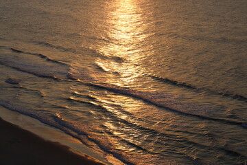 The sun illuminates the sky creating golden ripples of waves that brush along shore