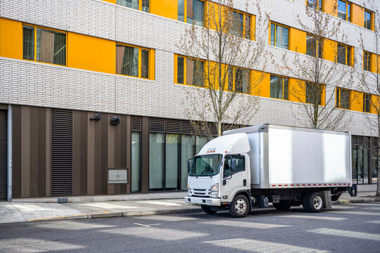 Small compact cab over truck with box trailer delivering cargo to multilevel urban city apartments