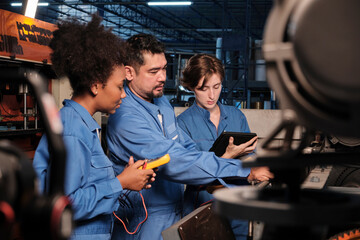 Multiracial professional industry engineer teams in safety uniforms work by inspecting machines' voltage current, checking, and maintaining at manufacture factory, electric system service occupations.