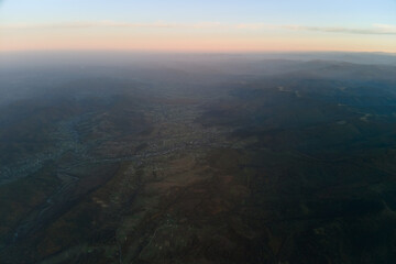 Aerial view of dark mountain hills with bright sunrays of setting sun at sunset. Hazy peaks and misty valleys in evening