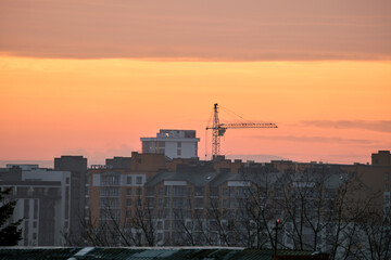 Fototapeta premium Dark silhouette of tower cranes at high residential apartment buildings construction site at sunset. Real estate development